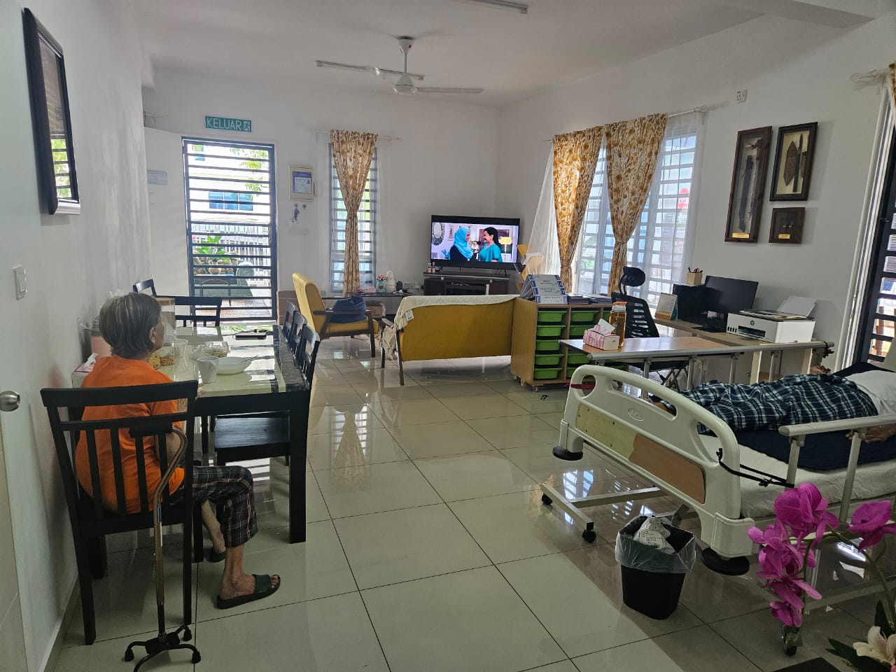 Pusat Jagaan Warga Emas Gerbang Dzunnurayn common area - resident at dining table, TV lounge, and hospital bed